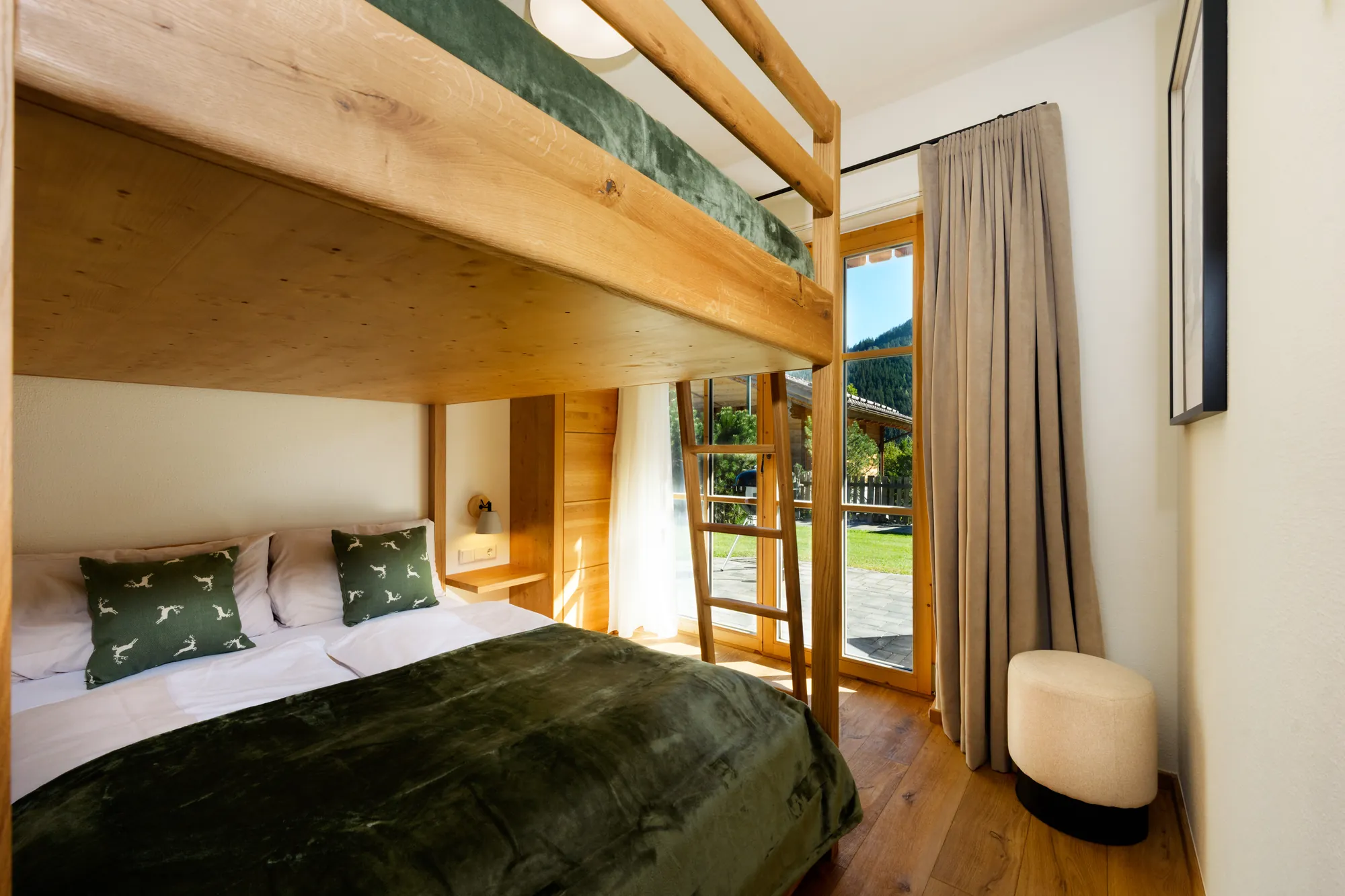 Etagenbett aus Holz mit zwei 140 cm breiten Liegeflächen, grüner Bettwäsche und Fenstertür ins Grüne